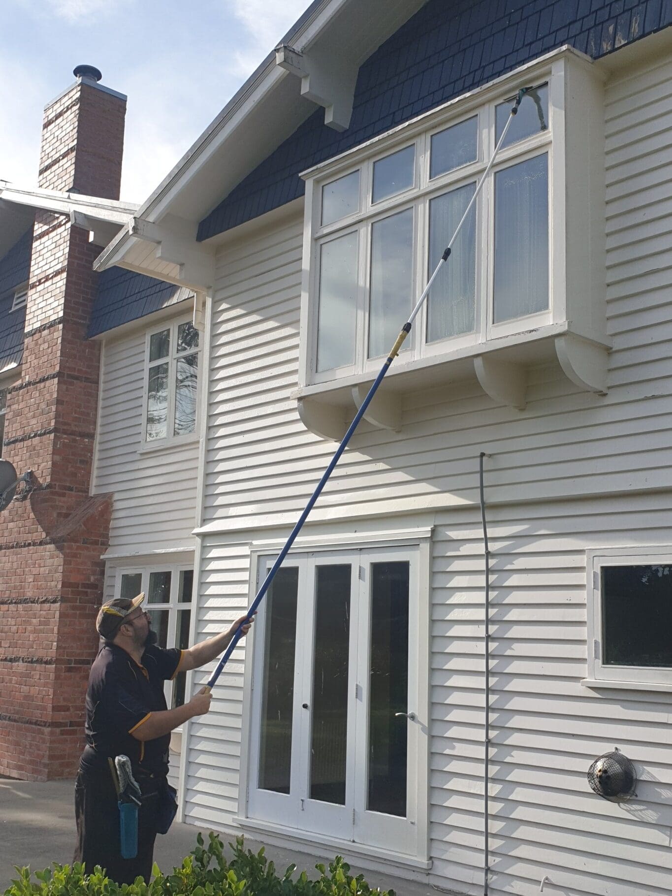 Professional cleaner using an extendable tool to clean upper-story windows of a house in Christchurch